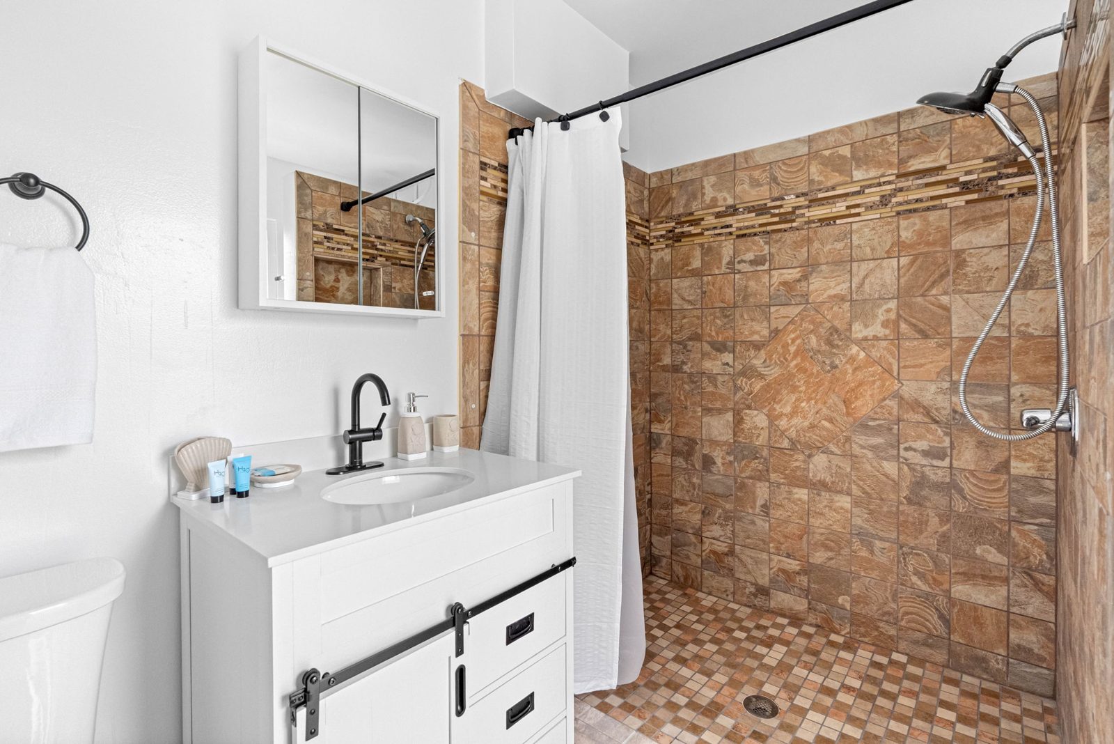 The tiki-side bathroom with a white vanity and a large tiled walk-in shower